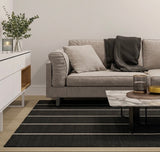 Alfombra Petra Charcoal Sand de polipropileno, negra con líneas claras, en living con sofá gris