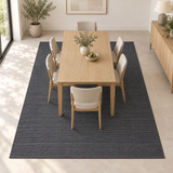 Alfombra Basai Gunmetal de polipropileno gris oscuro en comedor con mesa de madera