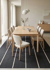 Alfombra Petra Charcoal Sand de polipropileno bajo mesa de comedor de madera clara