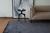 Alfombra Komara Dark Grey de Tencel junto a sillón beige y mesa lateral negra