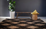 Alfombra Trenza Black de cáñamo en ambiente con banca de madera y muro oscuro