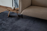 Alfombra Komara Dark Grey de Tencel junto a sillón beige